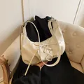 Schicke beige Hobo-Tasche aus glänzendem Lackleder mit Bandschleife auf einem Sofa - Weiß