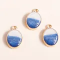 Detailed view of three gold-rimmed oval resin pendants with blue shimmer and white finish - Blue