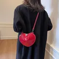 Elegante bolso bandolera rojo con forma de corazón llevado sobre un blazer negro de mujer - Rojo