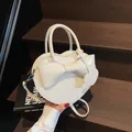 White heart-shaped handbag with decorative bow and crossbody strap on a dark wooden background - Off-white