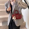 Chic burgundy patent leather crossbody bag with plush charm and gold hardware on grey suit - With Pendant / Red