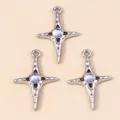 Three silver-tone star cross pendants with iridescent central gems on beige background - Silver