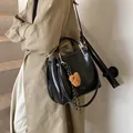 Black glossy tote bag with gold handles and bear charm worn by model in trench coat - With Pendant / Black