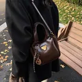Dunkelbraune glänzende Eimertasche mit Metalldreieck und gewebtem Anhängerriemen - Mit Anhänger / Braun