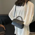Chic black leather crossbody bag with gold lettering and top handle on a model - Black