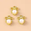 Three gold bow pendants with pearls for DIY jewelry making on a warm beige background - Pearl Flower