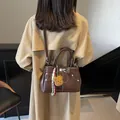 Sac Kelly marron foncé en cuir avec boucle argentée et coutures blanches - Café Avec Pendentif