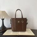 Borsa a secchiello marrone scuro con dettagli dorati e tracolla su un libro - Solo Borsa / Marrone