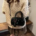 Glossy black patent leather top handle bag with bow accent and heart charm detail - Black