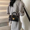 Glossy black shoulder bag with gold hardware and charm on a model in gray blazer - Black With Rabbit Pendant