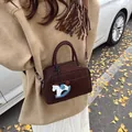 Dark brown rectangular Boston bag with a horse pendant shown on a street with ginkgo leaves - Brown