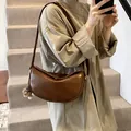 Brown faux leather half-moon crossbody bag with plush charm on a model in neutral setting - With Pendant / Brown