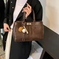 Vintage brown tote bag with baseball charm and silver twist lock in hand - Coffee With Pendant