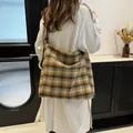 Brown plaid hobo tote bag shown on model wearing a trench coat in a minimalist room - Large / Yellow Plaid Style