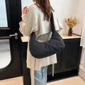Modern black quilted puffy crescent shoulder bag worn with a light trench coat - Black