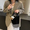Modische schwarze Beuteltasche mit Bärenanhänger am Model in moderner Café-Umgebung - 24cmx14cmx29cm / Schwarz