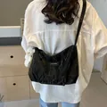 Black glossy tote bag with crinkle texture and cute plush bear charm on model shoulder - Black