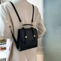 Sac à dos minimaliste en similicuir noir avec boucles dorées porté par un mannequin - Noir