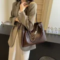 Bolso tote marrón oscuro con asas trenzadas y cadena de perlas mostrado en modelo - café