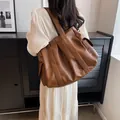 Brown faux leather large tote bag with wide strap shown on a shoulder in a cozy setting - Brown