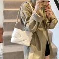 Minimalist beige underarm bag with woven side details shown on a model on stairs - White