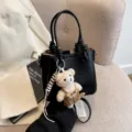 Schwarze Beuteltasche aus Leder mit beigem Plüschbären-Anhänger und verstellbarem Riemen - Mit Anhänger / Schwarz