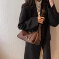 Braune Umhängetasche aus Leder mit breitem Gurt und goldenen Details auf schwarzem Blazer - Braun