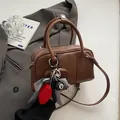 Braune Vintage Leder Boston Handtasche mit Anhängern auf einem grauen Blazer-Anzug - 24*8*13cm / Braun + Anhänger