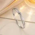 Polished titanium steel knot bangle with sparkling crystals on warm silk backdrop - Steel