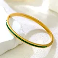 Luxurious gold titanium bracelet featuring square-cut green zircons on a stone background - Eternity Green Zirconia Bangle / Gold