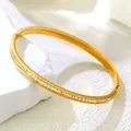 Detail of gold titanium bangle featuring a single row of square zircon stones and a side clasp - Eternity White Zirconia Bangle / Gold