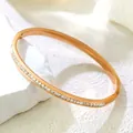 Close-up of a rose gold titanium steel bangle with sparkling zircons on a white stone - Eternity White Zirconia Bangle / Rose Gold