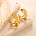 Detail von dreireihigen Wellen-Creolen in poliertem Gold auf beigem Steinuntergrund - Dreilagiger Paralleler Wellenförmiger Breiter Stil (ED051) / Gold