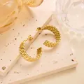 Details von gedrehten, vergoldeten Ohrringen auf beigem Steinboden-Hintergrund - Mehrsträngiger Spiralgedrehter C-Form-Stil (ED064) / Gold