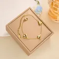 Elegant gold titanium steel bracelet featuring three polished heart charms on a beige case - Triple Heart Bracelet (SL5088J) / Gold