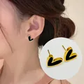Detailed view of heart-shaped gold-framed black enamel stud earrings worn on ear - Black Heart Stud Earrings Pair