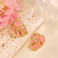 Close-up of pink monstera leaf earrings with gold trim on a stylish textured background - Pink