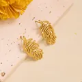 Detailed close-up of golden hollow leaf earrings on a textured stone surface - Hollow Out Feather (ED204) / Gold