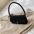 Minimalist black leather underarm bag with gold metal clasp on a soft fabric background - Black