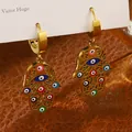 Détail des boucles d'oreilles Main de Fatma avec breloques œil bleu en acier doré - Boucles d'oreilles Hamsa Œil du Mal ajourées avec strass multicolores