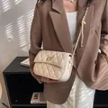 Elegante beige gewatteerde kettingtas met gouden draaislot gedragen door een model - Groot / Wit