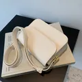 Bolso de hombro crema minimalista con hebilla dorada cuadrada sobre un libro blanco - Blanco Roto