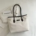 Minimalistische beige Tragetasche mit schwarzen Trägern auf einem lässigen Blazer-Hintergrund - Weiß & Schwarz
