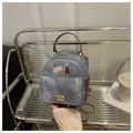 Détail d'un mini sac à dos en denim avec écussons chat et fermoir doré sur support - Gris