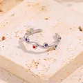Détail d'une bague ondulée en acier argenté avec zircons colorés sur socle beige - Ouvert / Argent/Zircone AB