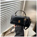 Close-up of black glossy leather handbag with vintage bronze lock and adjustable strap - Black