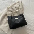 Black quilted tote bag with chain strap and brand plate displayed on a chic background - White