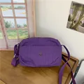Violette karierte Canvas-Umhängetasche mit Silberlogo auf einem Holztisch - Lila