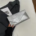 Metallic silver crocodile pattern envelope clutch bag held against a grey suit - Silver