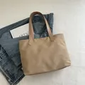 Minimalist khaki nylon tote bag with reinforced handles laid flat on a blue denim jacket - Khaki